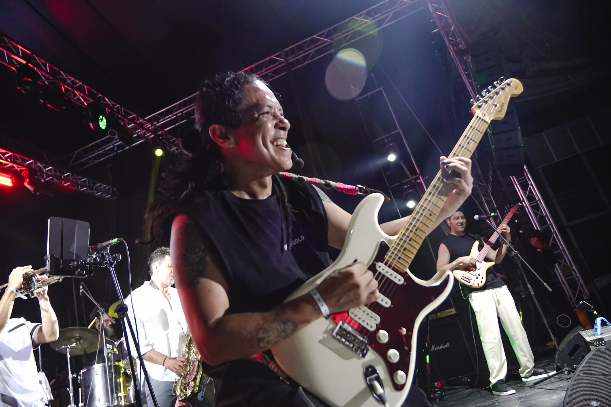 Johan Villamil sonríe mientras toca la guitarra, con músicos de la banda detrás